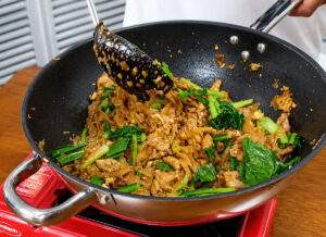 Cuisson du Pad See Ew au wok avec nouilles de riz, poulet et brocoli chinois.