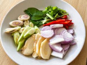 Citronnelle, galanga, échalotes, feuilles de combava, coriandre et piments rouges préparés pour un Tom Yam Nam Khon.