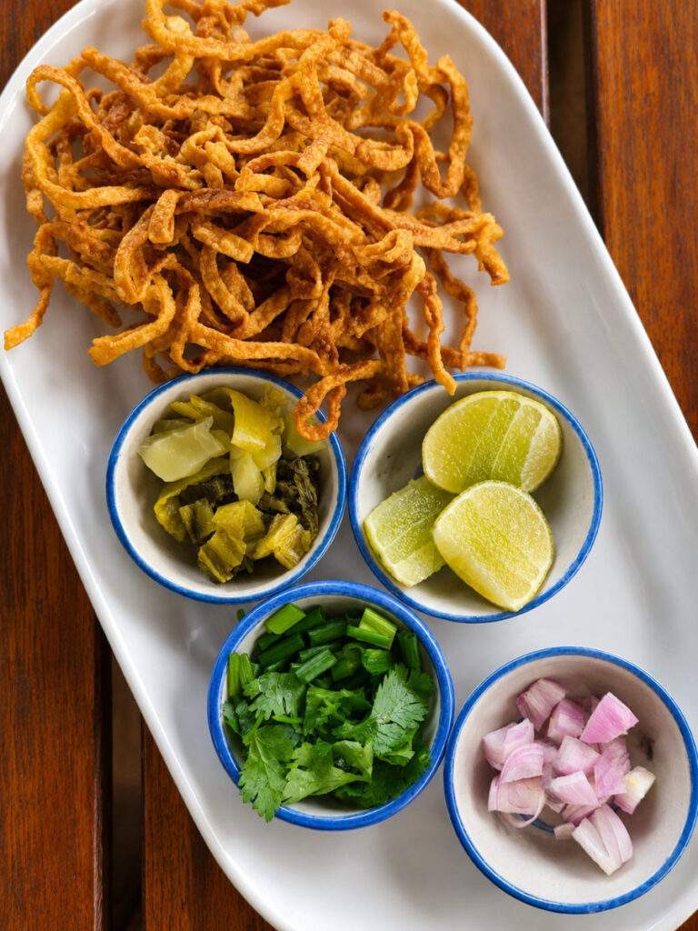 Condiments du Khao Soi avec citron vert, échalotes, coriandre, légumes marinés et nouilles croustillantes