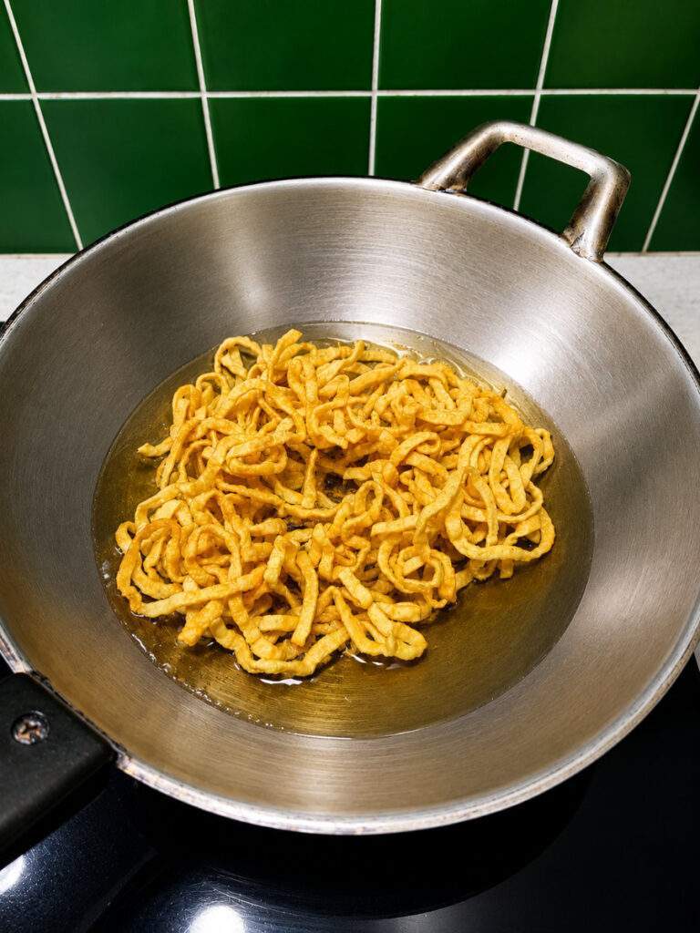 Nouilles aux œufs en train de frire dans un wok pour préparer les nouilles croustillantes du khao soi thaïlandais.