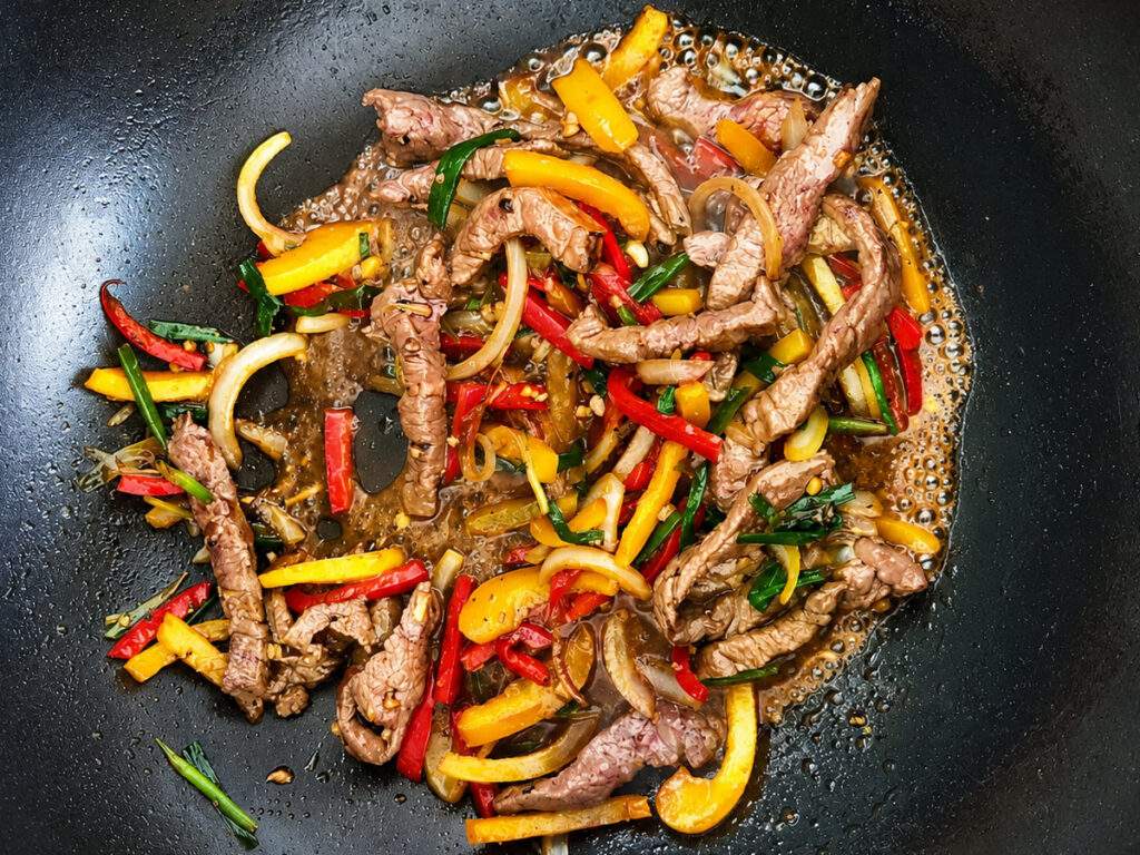 Préparation d'un bœuf au poivre noir thaï dans un wok avec poivrons et basilic thaï.