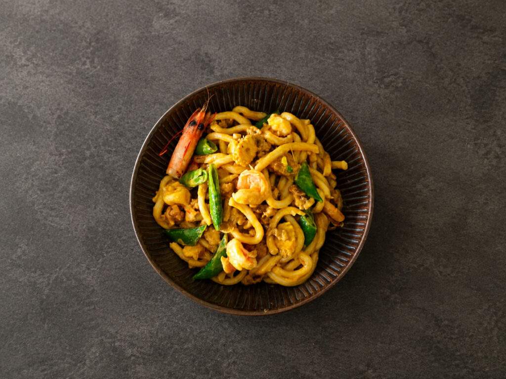 Bol de nouilles udon au curry jaune avec poulet, crevettes et pois gourmands
