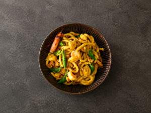 Bol de nouilles udon au curry jaune avec poulet, crevettes et pois gourmands