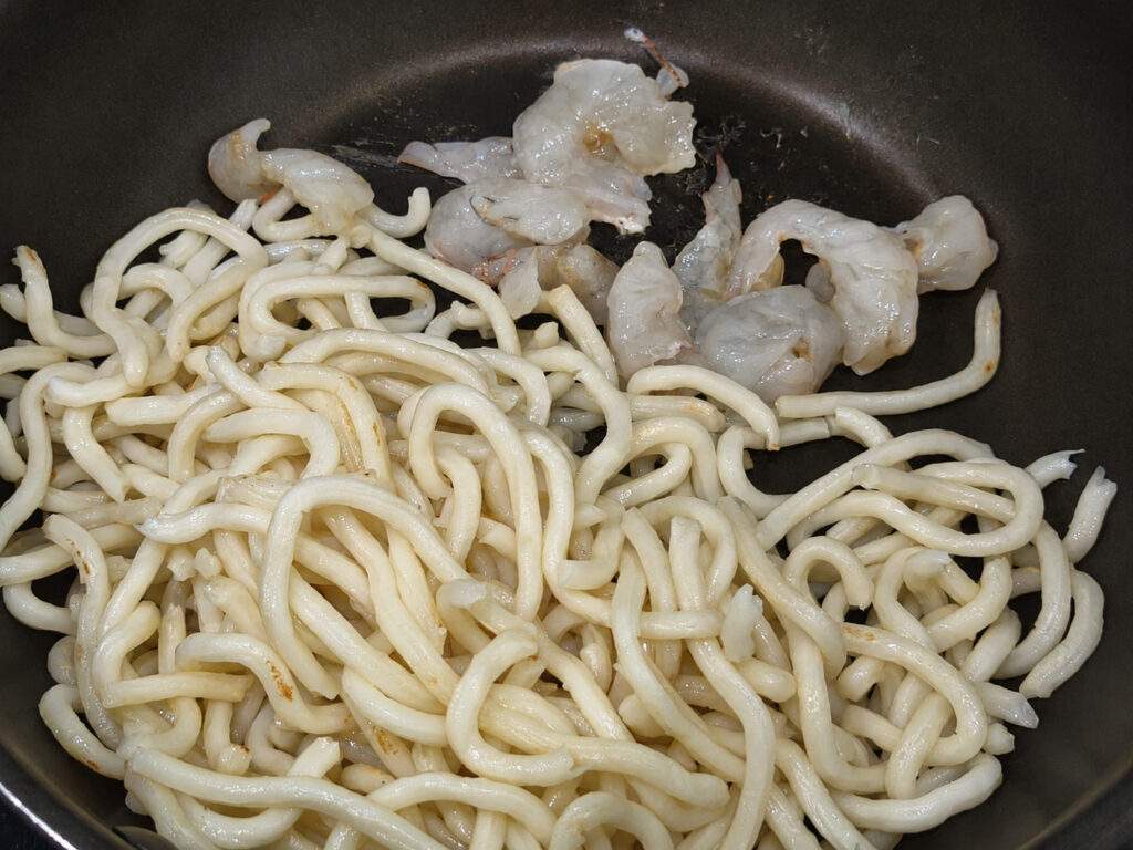 Nouilles udon et crevettes crues placées dans une poêle